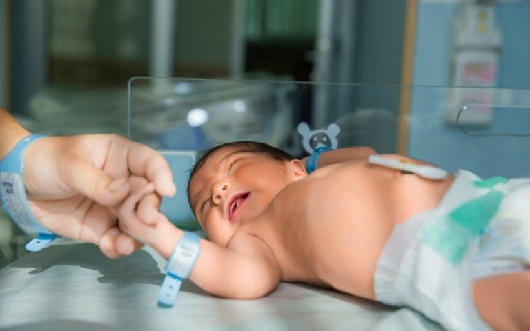 father holds hand of newly born babe in diapers