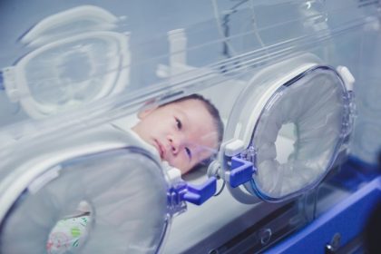 Newborn baby boy covered in vertix inside incubator.