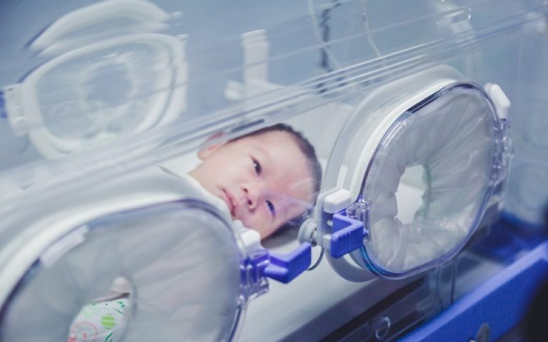 Newborn baby boy covered in vertix inside incubator.